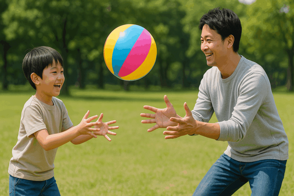 公園の芝生で、私服姿の日本人の父親と男の子がカラフルなビニールボールを使って笑顔で遊んでいる様子。明るい日差しと緑に囲まれた自然の中、親子が楽しそうに向かい合っている。